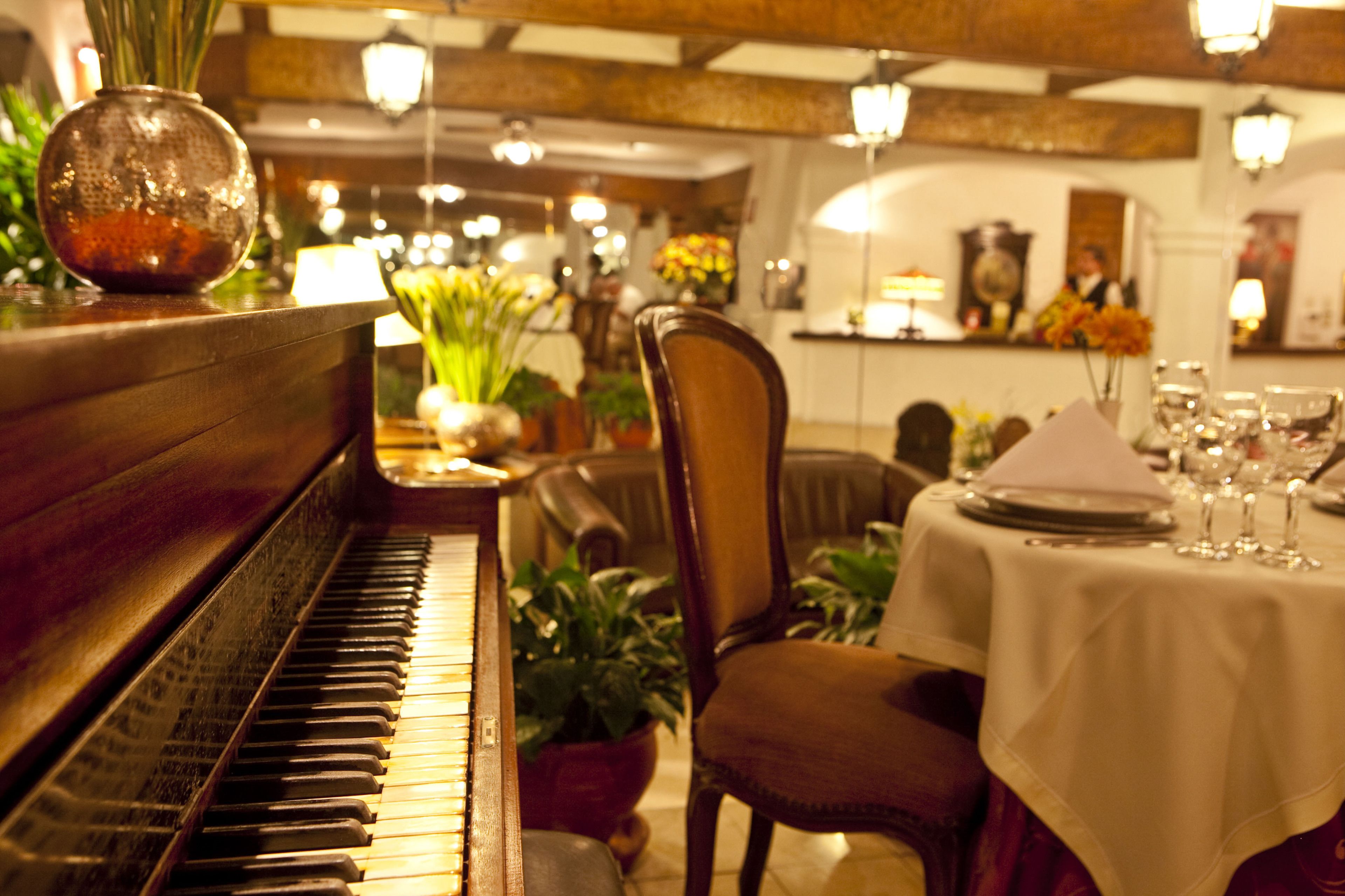 A piano, a dining table set with plates and glasses, and a chair.