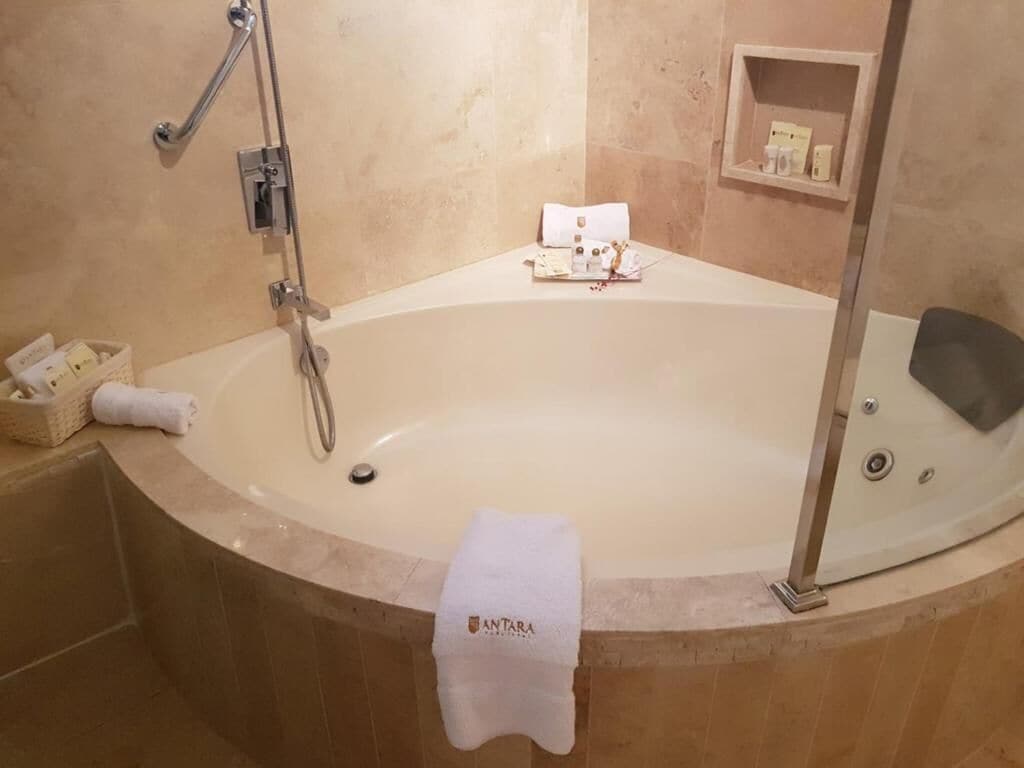 A bathroom with a bathtub, a shower, and a shelf with toiletries.