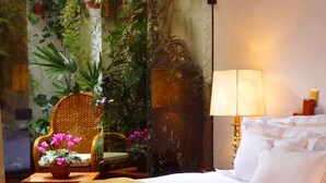 Une chambre d’hôtel avec un lit, une chaise en osier décorée de fleurs, une table de chevet et une lampe.