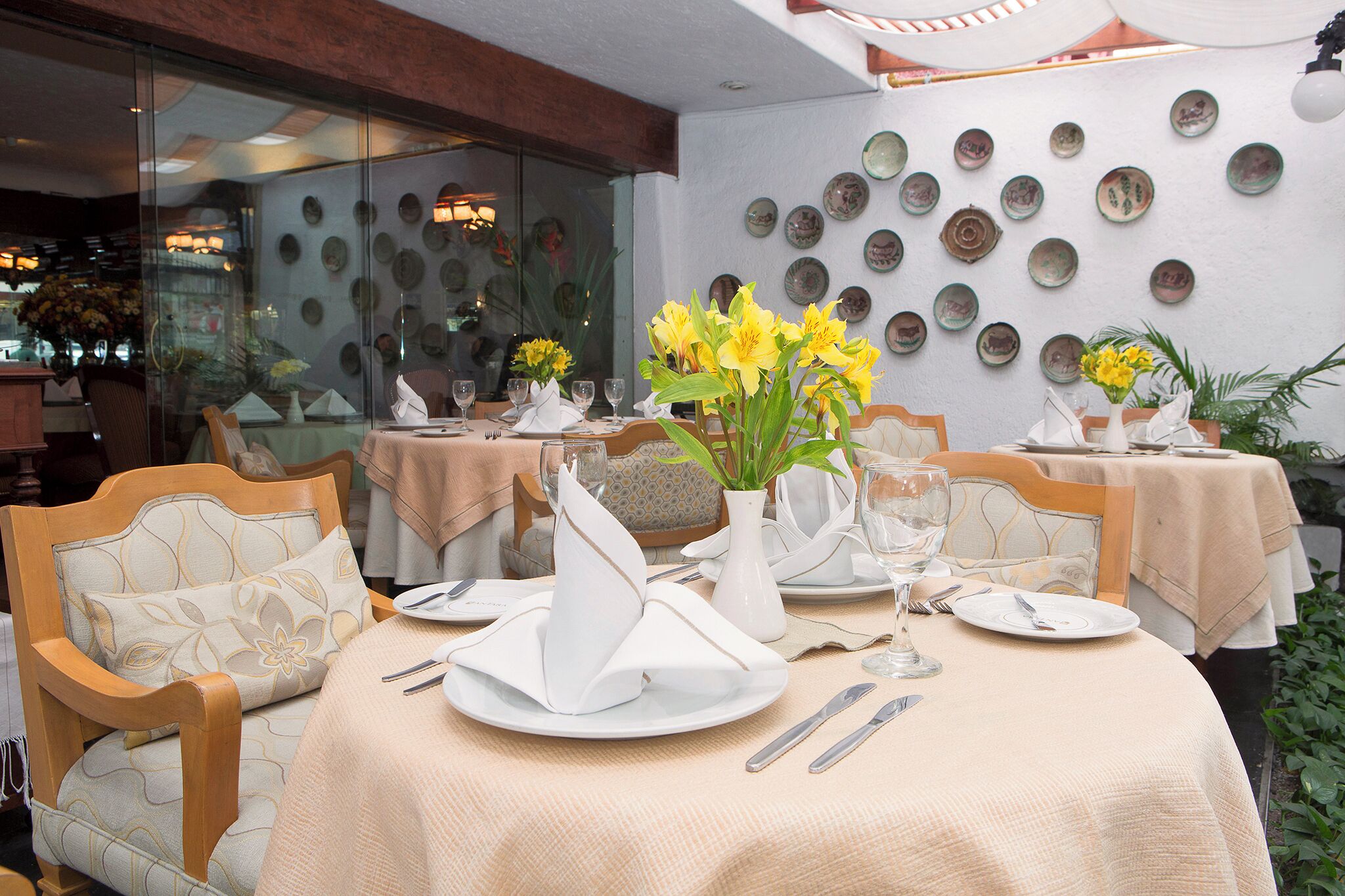 Un comedor con mesas redondas, servilletas blancas y flores amarillas.