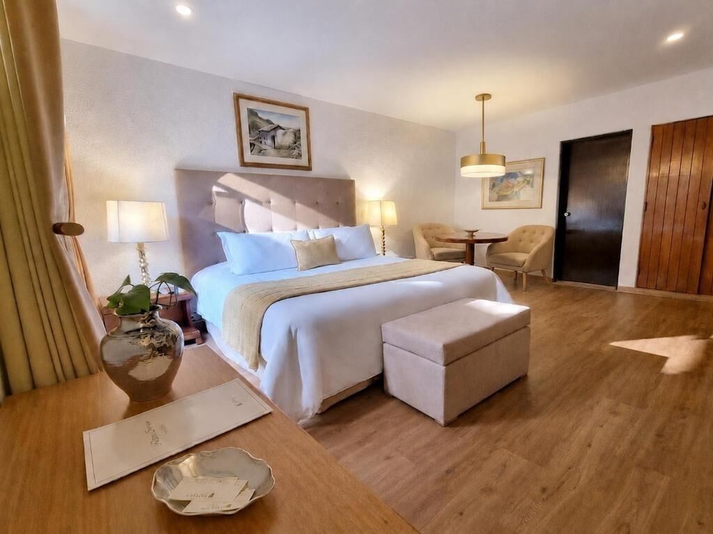 A hotel room with a bed, bedside tables, a chair, a desk, a lamp, and a door.