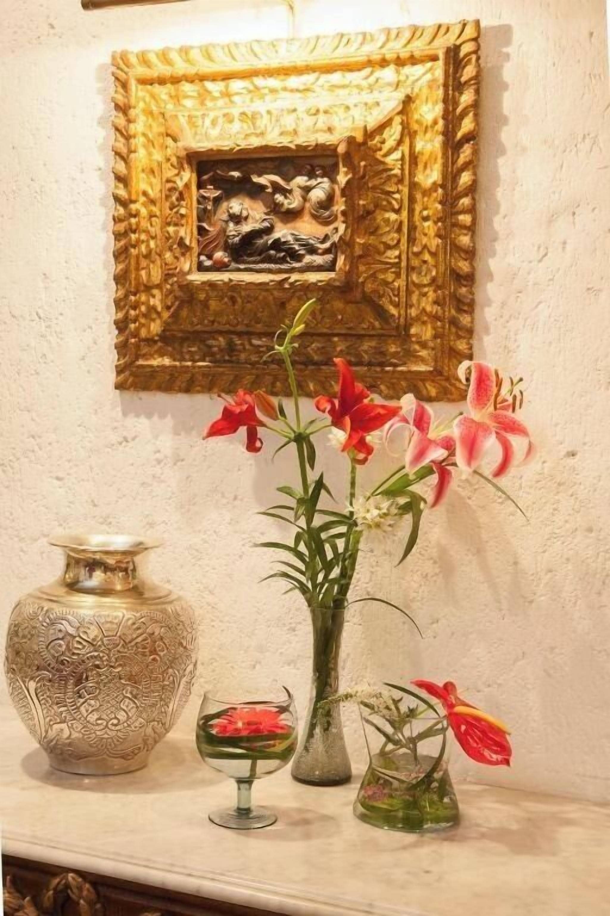 A wall with a framed artwork, a large ornate vase, and three smaller vases with flowers.