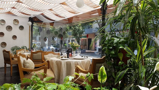 Un espace de restauration intérieur accueillant, avec des meubles en bois, une table dressée pour deux personnes et une vue sur la rue grâce à de grandes fenêtres.