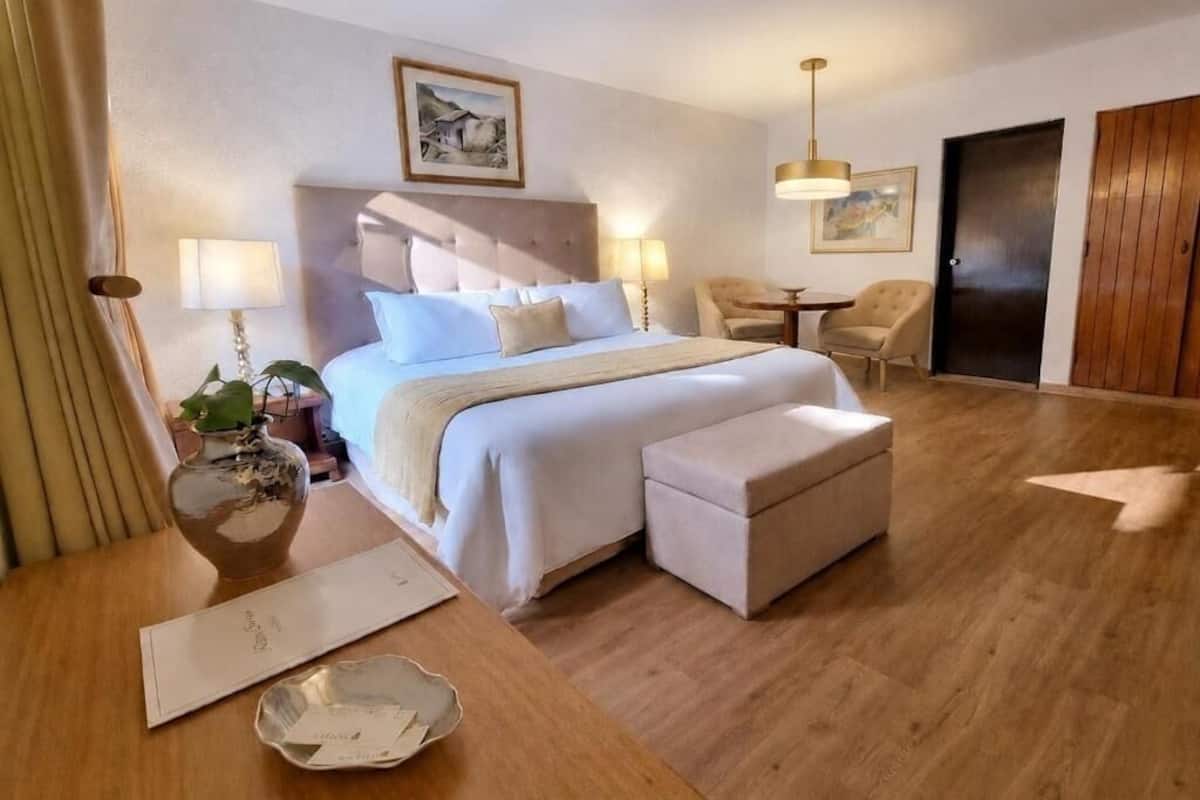 A hotel room with a bed, bedside tables, a chair, a desk, a lamp, and a door.