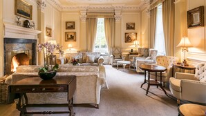 A spacious living room with a fireplace, multiple seating areas, and a large window with curtains. - Eshott Hall (Morpeth)