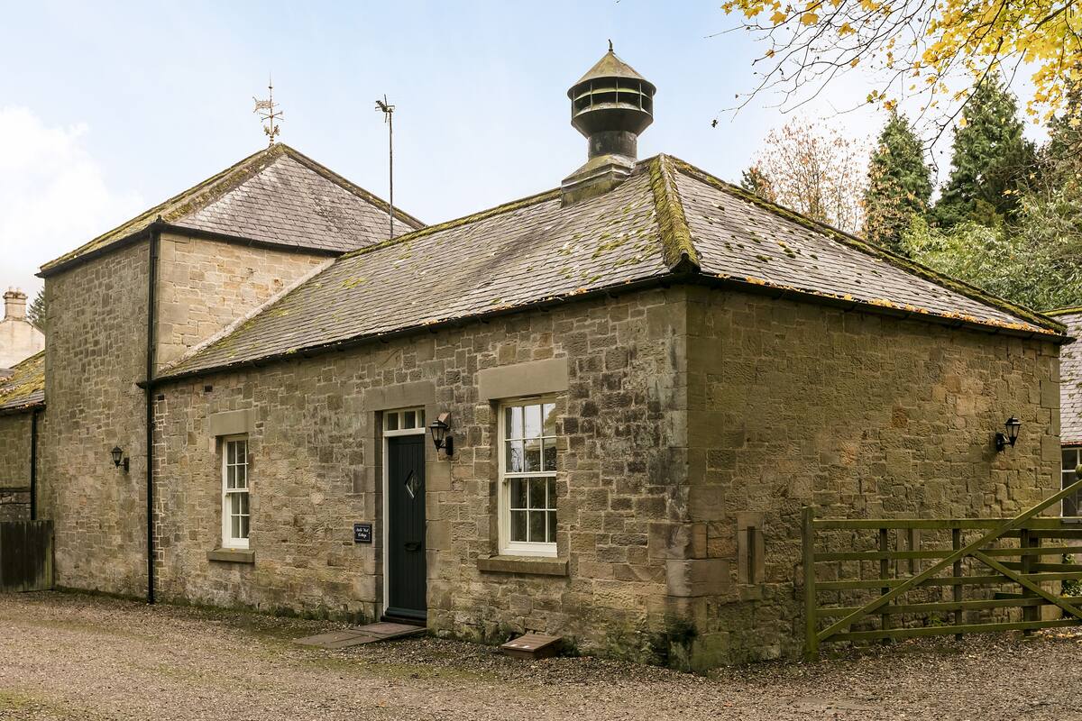 A stone building with a black door, two windows, and a small tower-like structure on the roof.