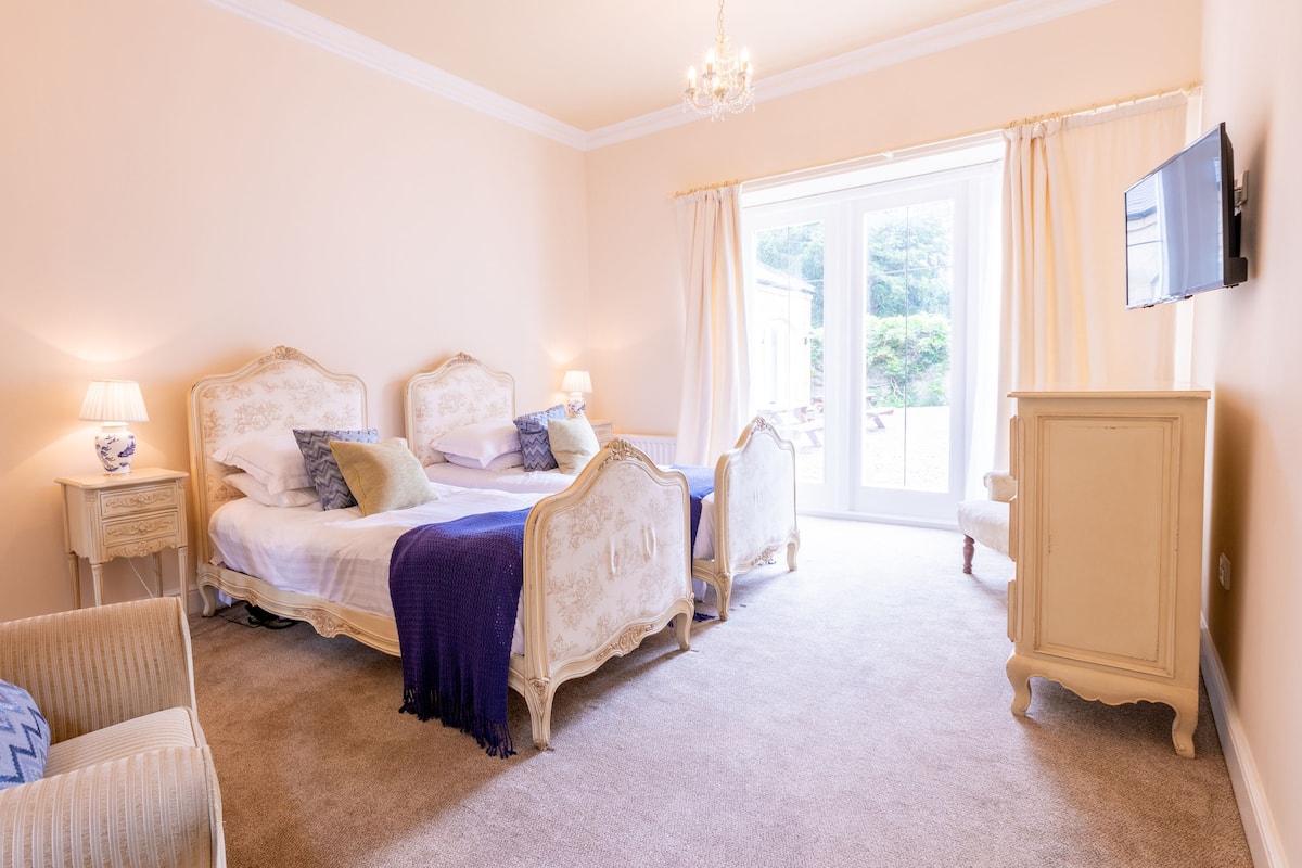 A bedroom with two ornate beds, a nightstand, a chair, a wardrobe, and a television on the wall.