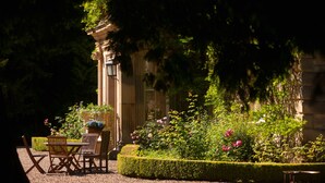 A garden with a table and chairs, a fountain, and a building with columns. - Eshott Hall (Morpeth)