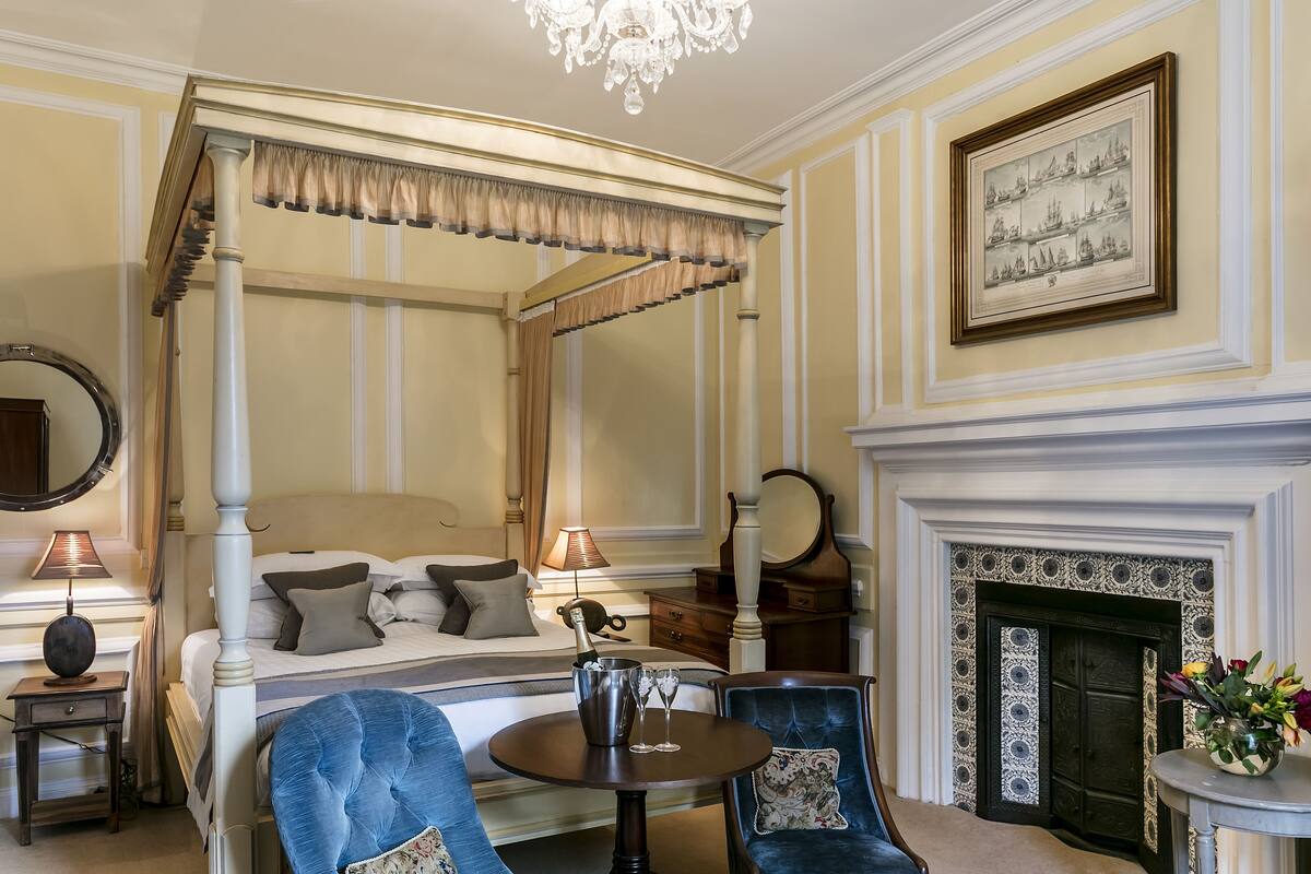 A four-poster bed with a canopy, a fireplace, a chandelier, and a framed picture on the wall.