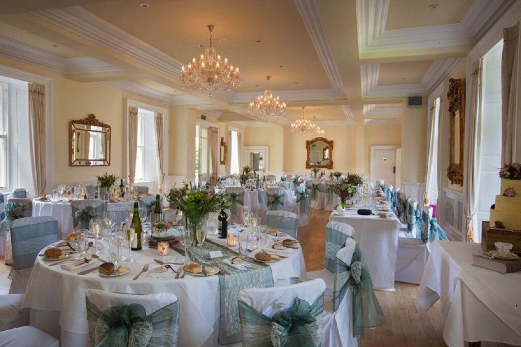 A banquet hall with round tables set for a formal event, featuring chandeliers, white tablecloths, and blue chair covers.