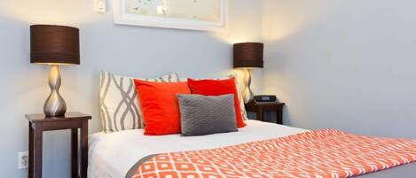A neatly made bed with a patterned blanket, two bedside lamps, and a framed artwork on the wall.
