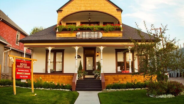 A two-story house with a porch, a front entrance, and a signboard. - Boise Guest House (Boise)
