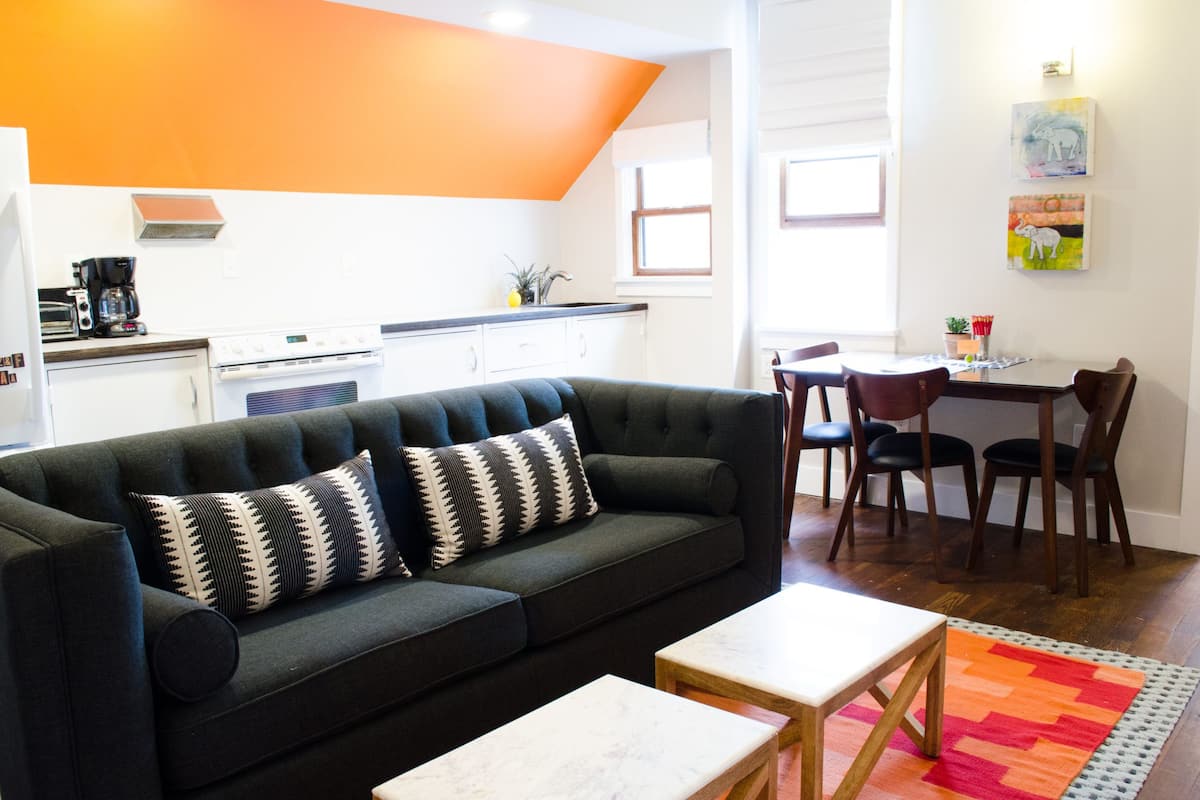A modern living room with a dark green sofa, a white coffee table, and a colorful rug.