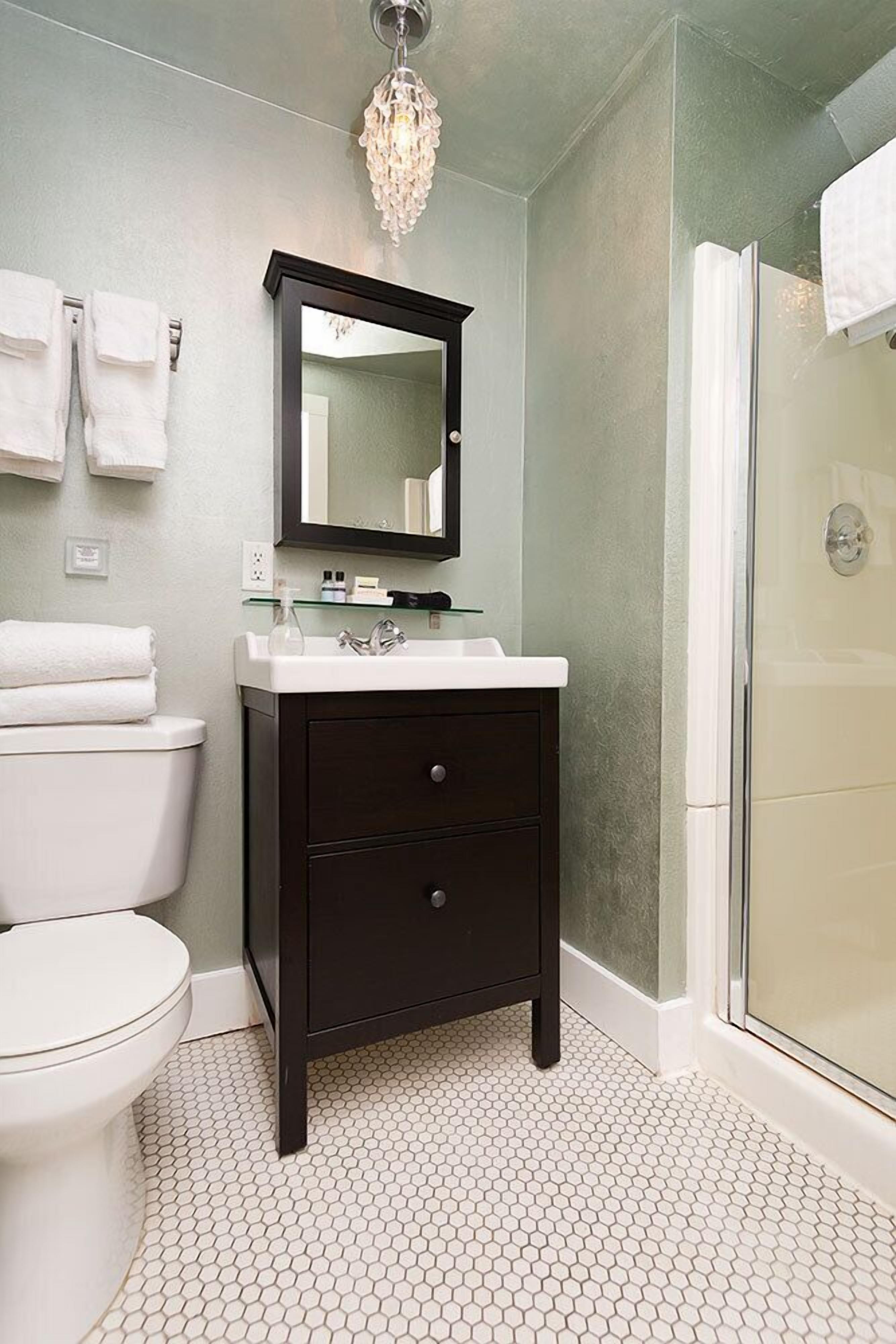 Een badkamer met een wit toilet, een donkere wastafel met spiegel, een douchecabine van glas en zeshoekig betegelde vloertegels.