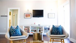 A living room with two armchairs, a coffee table, a TV, and a bookshelf. - Boise Guest House (Boise)