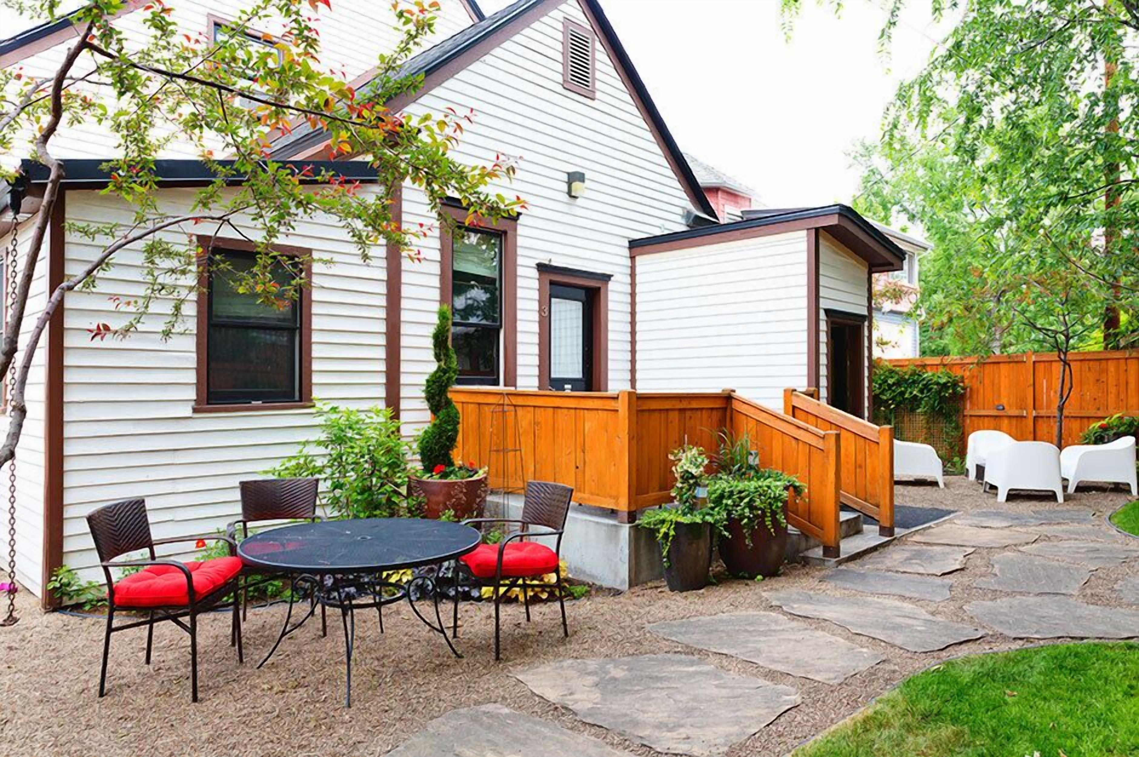 A house with a patio area featuring a round table and chairs, a wooden deck, and a stone pathway.