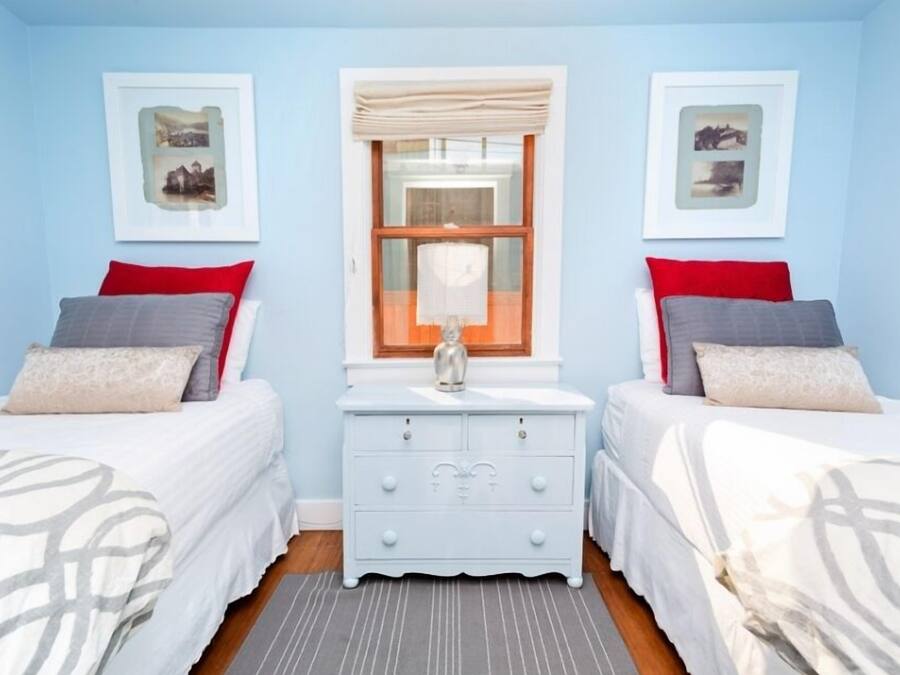 A bedroom with two beds, a dresser, and a window with curtains.