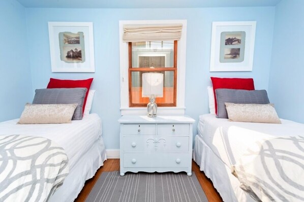 A bedroom with two beds, a dresser, and a window with curtains.