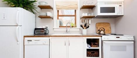 Una cocina compacta con electrodomésticos blancos, armarios de madera y una ventana con vistas.