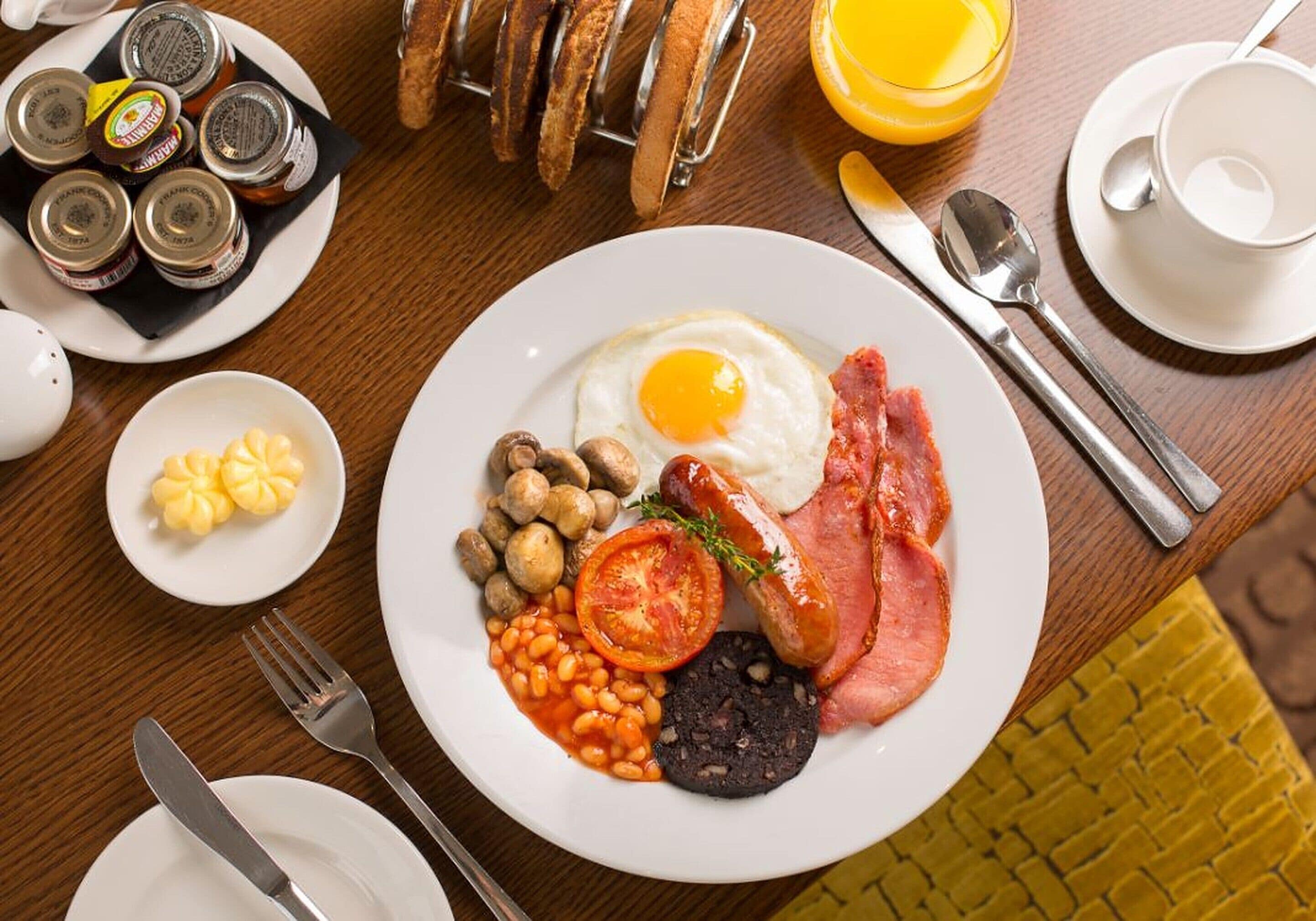 A breakfast plate with eggs, bacon, sausages, mushrooms, beans, tomato, and black pudding.