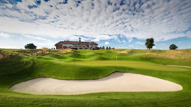 Un campo de golf con un búnker de arena, un club de campo y un árbol grande.