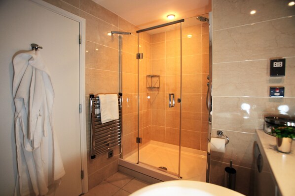 A modern bathroom with a glass-enclosed shower, a white bathtub, and a towel rack with multiple towels.