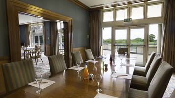 A conference room with a long table, chairs, and a view of the outdoors through large windows.