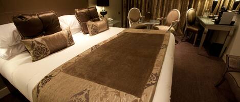 A hotel room with a large bed, a desk, a chair, a small table, and a mirror.