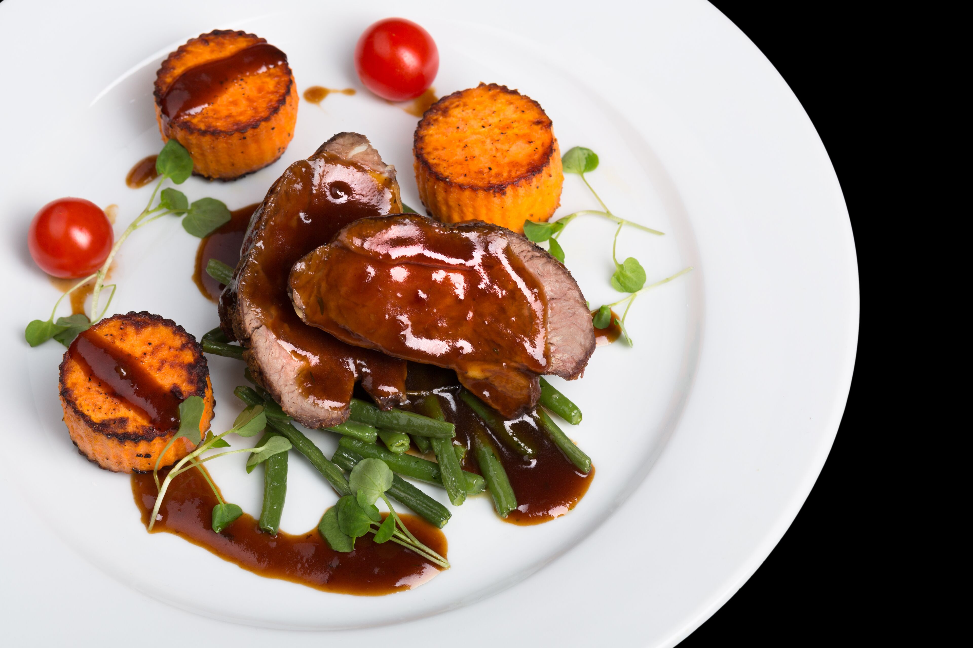 A plate of food with steak, roasted potatoes, green beans, and cherry tomatoes.