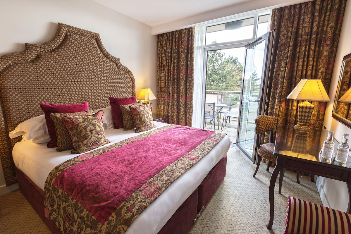 Ein Hotelzimmer mit einem großen Bett, einer Sitzecke mit Tisch und Stühlen sowie einem Balkon mit Aussicht.