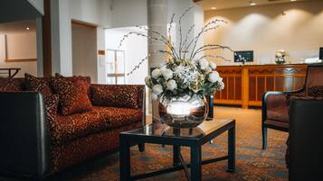 A lobby with a patterned sofa, a glass-top table with a floral arrangement, and a reception desk in the background.