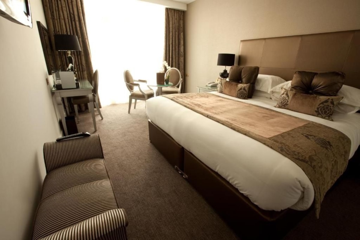 A hotel room with a large bed, a desk with a chair, a sofa, and a small table with a lamp.