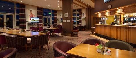 A hotel lobby with a bar area, dining tables, and comfortable seating.