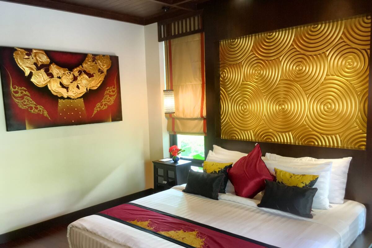 A hotel room with a bed, pillows, a nightstand, a vase with flowers, and a wall with a golden pattern.