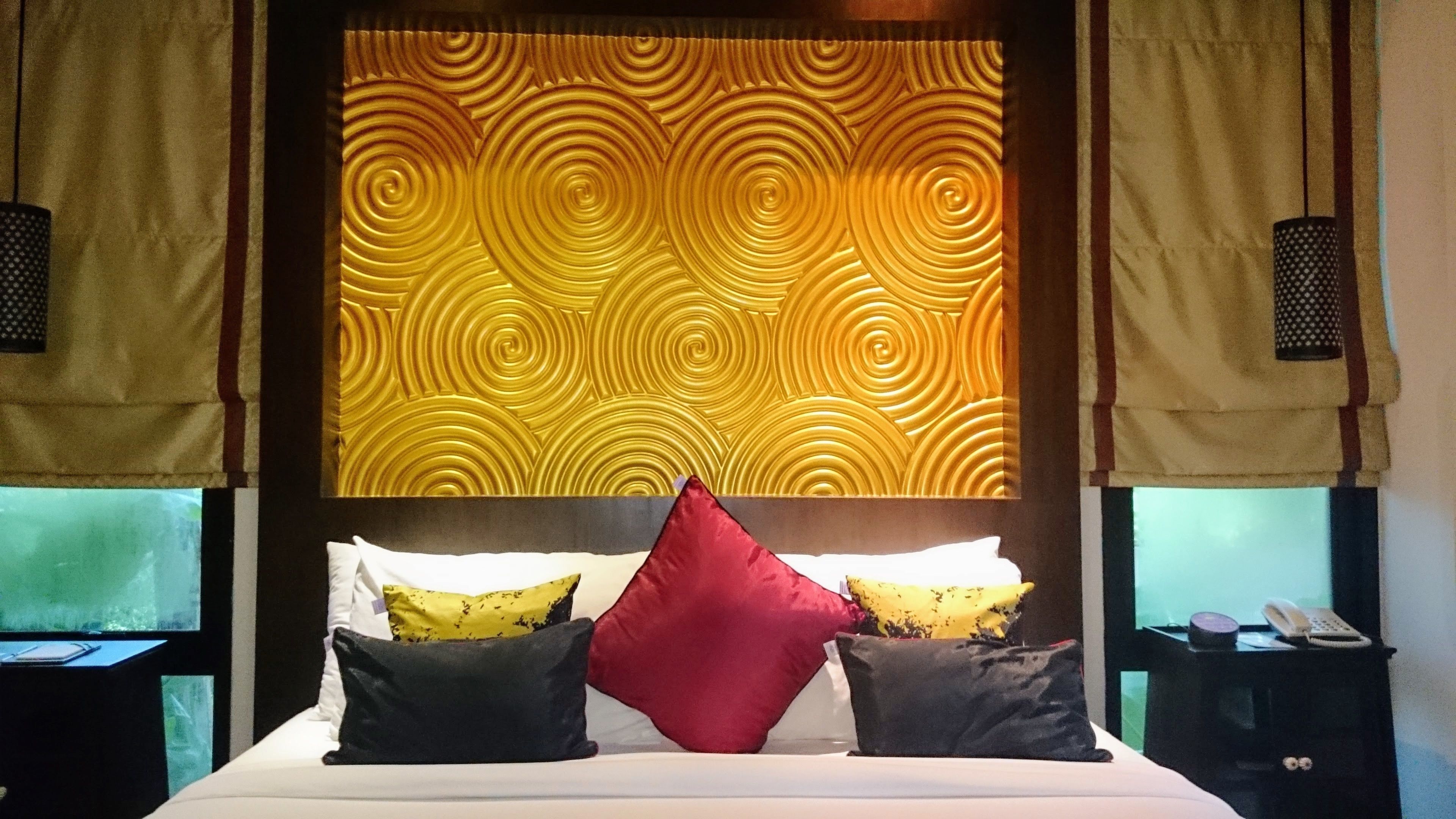 A hotel room with a bed, pillows, a nightstand, and a wall with a circular pattern.