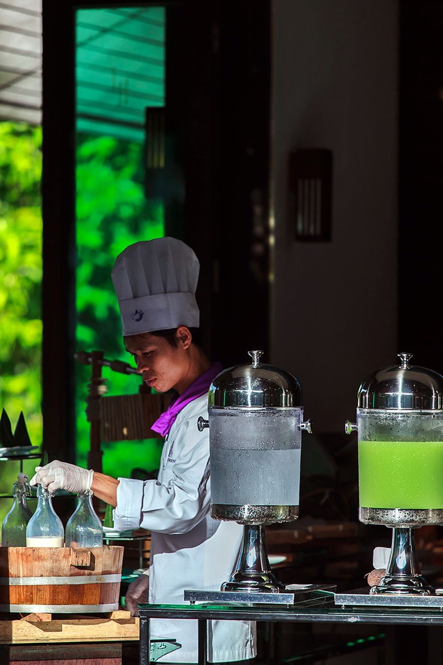 Un chef, vêtu d’un uniforme blanc, prépare des boissons en se concentrant sur un distributeur de boissons et un tonneau en bois.