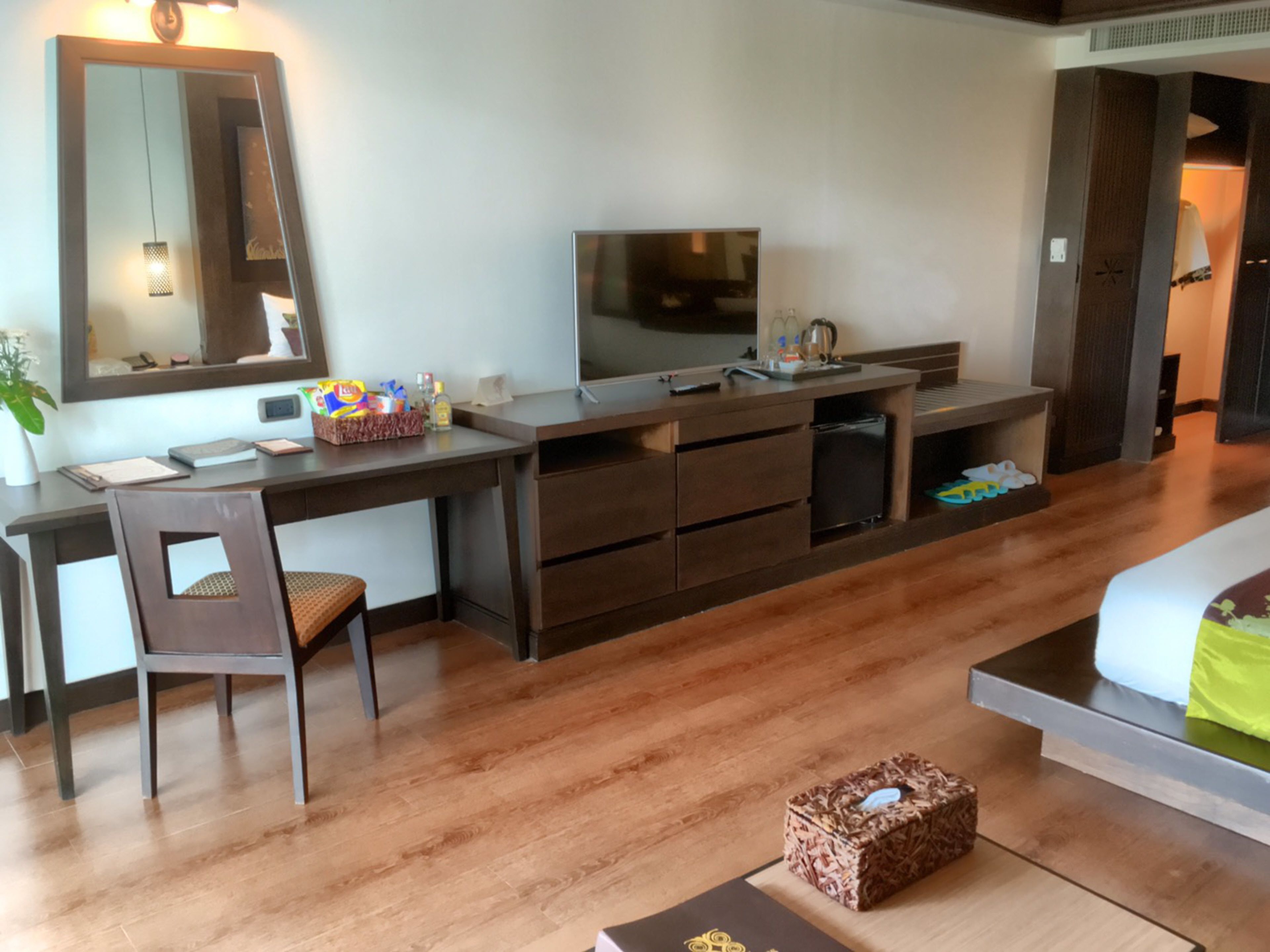 A hotel room with a wooden desk, a television, a bed, and a small table with a basket.