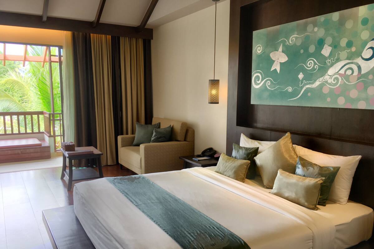 A hotel room with a large bed, a sofa, a desk, and a balcony with curtains.