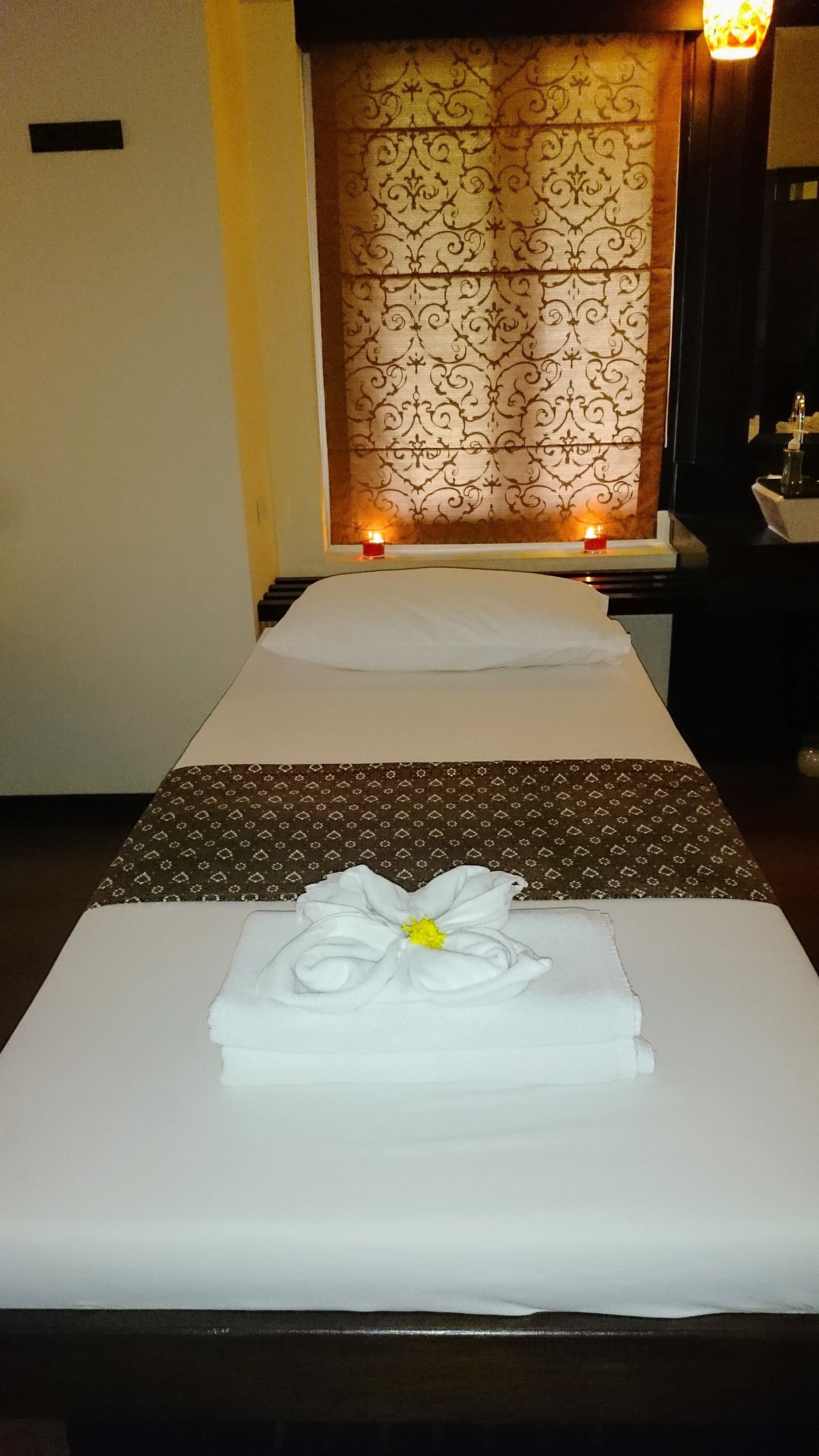 A massage table with a towel and flower decoration, a patterned curtain, and a small candle.