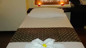A massage table with a towel and flower decoration, a patterned curtain, and a small candle.