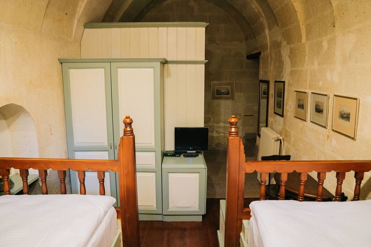 Ein Zimmer mit zwei Holzbetten, einem Fernseher auf einer Kommode und gerahmten Bildern an der Wand.