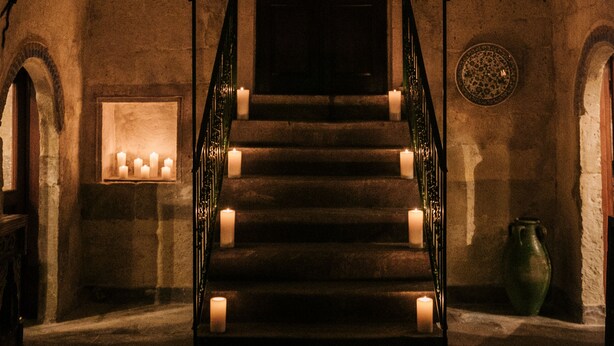 A grand staircase with a chandelier, candles, and a large vase in a stone-walled room.