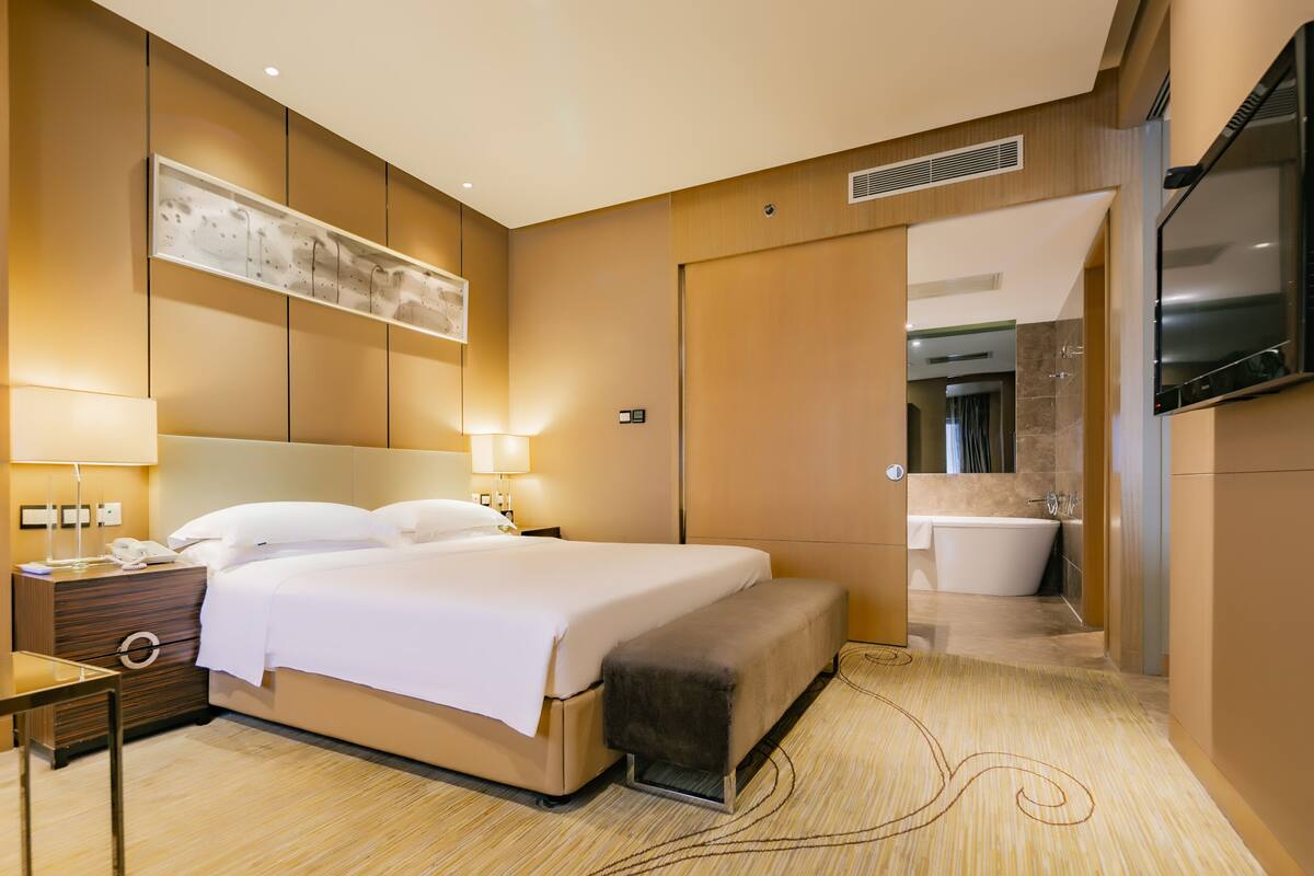 A modern hotel room with a large bed, bedside lamps, a desk, a TV, and a view of the bathroom.