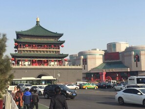 Un edificio chino tradicional con varios niveles y farolillos rojos, rodeado de edificios modernos y una calle concurrida con coches y peatones.