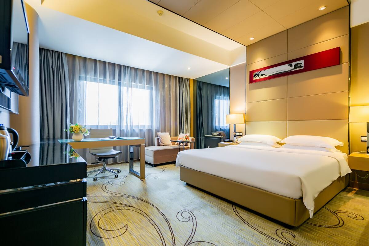 A hotel room with a large bed, a desk, a chair, and a sofa.