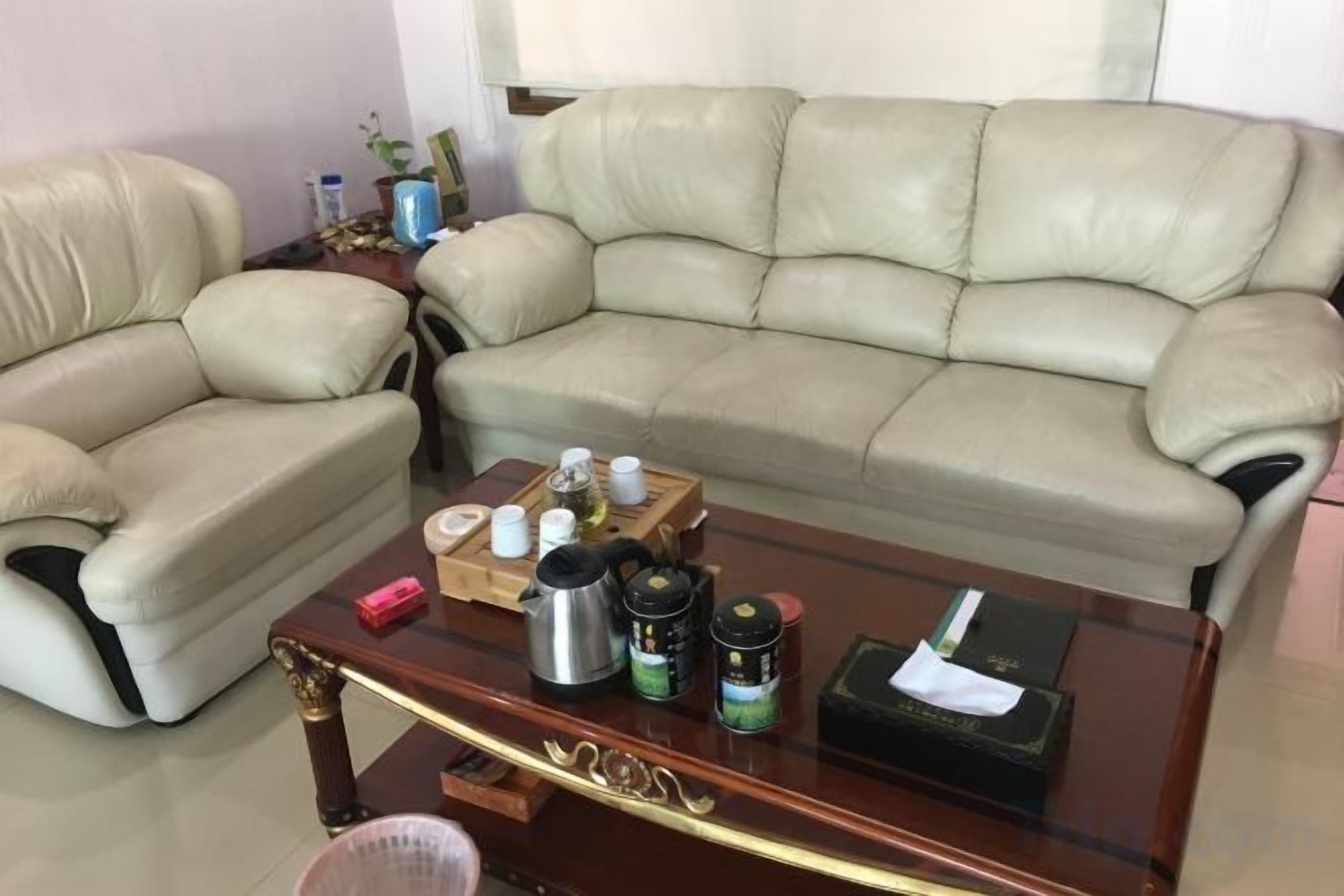 Una sala de estar con un sofá de cuero color beige, una mesa de centro de vidrio con varios objetos y una mesita de noche de madera.