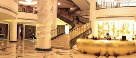 A spacious lobby with a grand staircase, marble columns, and a chandelier.
