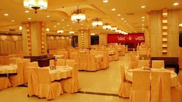 A banquet hall with round tables and chairs, a red carpet, and chandeliers.