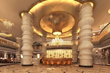 A grand lobby with large columns, a central reception desk, and a chandelier.. Century Palace Hotel