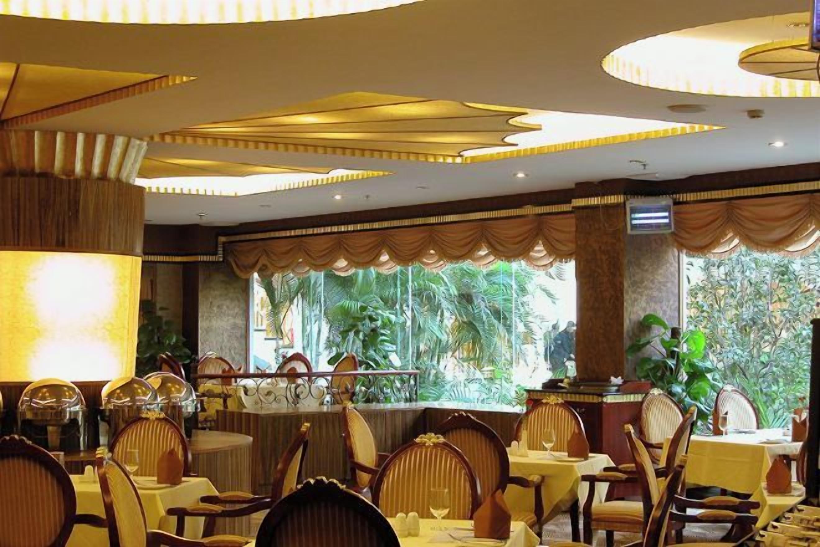 Un restaurante con mesas y sillas redondas, un ventanal con vistas a zonas verdes y un techo decorativo.